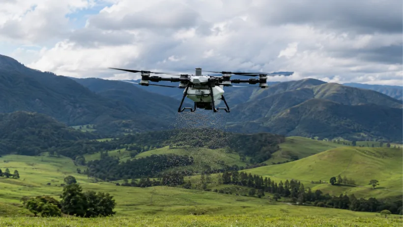A drone spreading granular fertiliser and seed over hill country