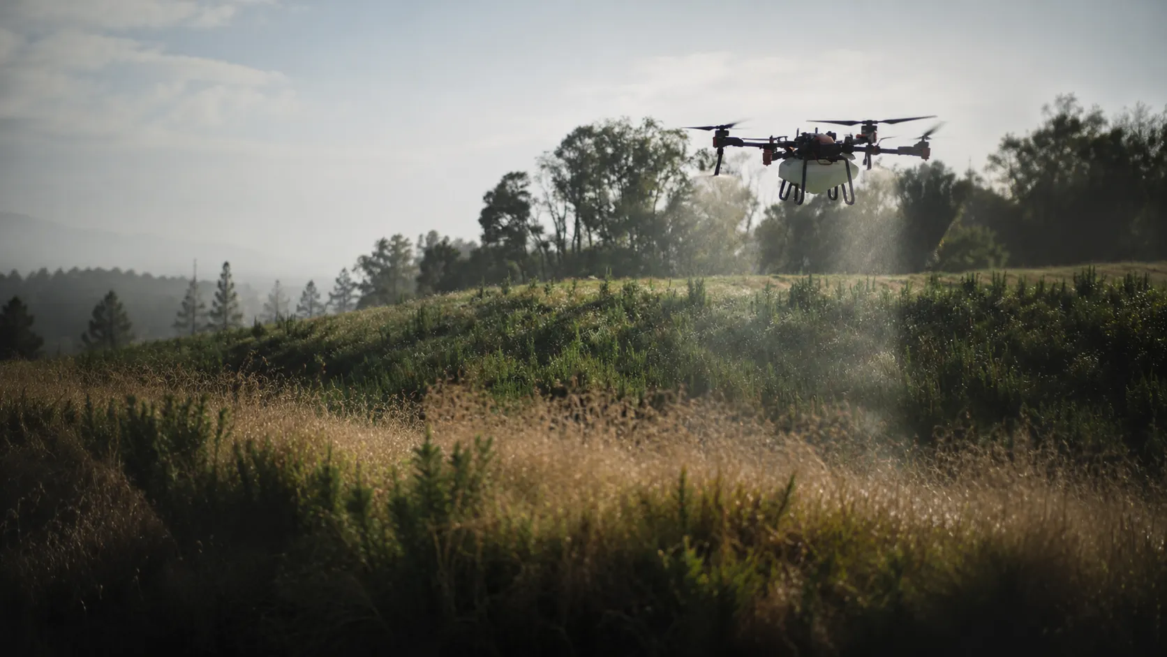 A Vantage spray drone working low over scrub hill country in golden evening light