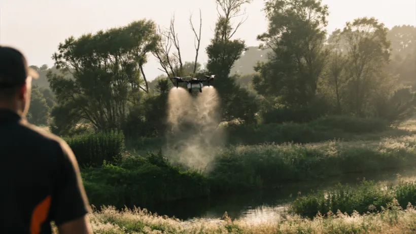 A drone applying low-drift weed control along a waterway
